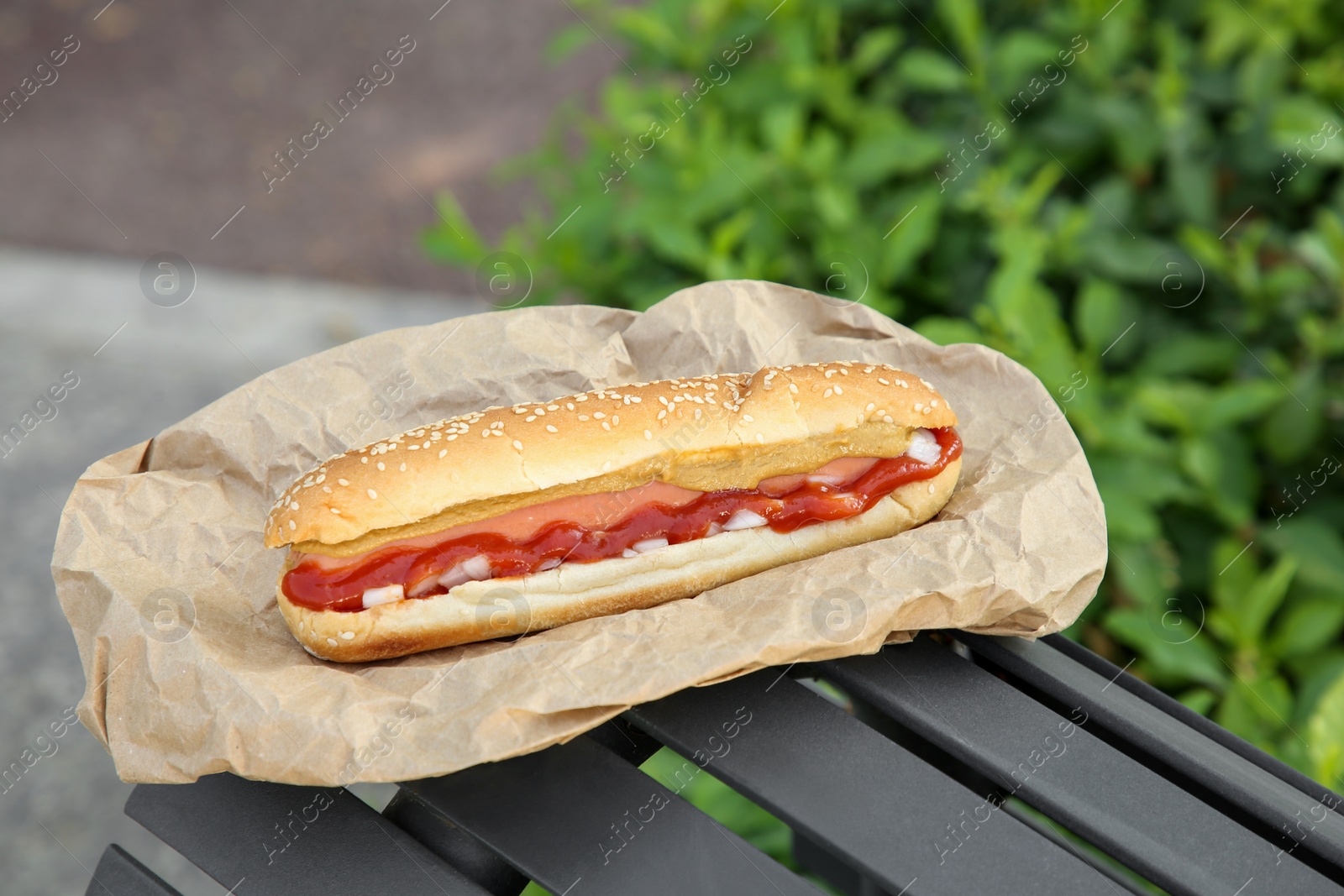 Photo of Fresh delicious hot dog with sauce on black bench outdoors