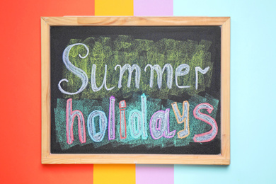 Photo of Chalkboard with phrase SUMMER HOLIDAYS on color background, top view. School's out