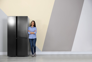 Photo of Happy young woman near refrigerator indoors, space for text