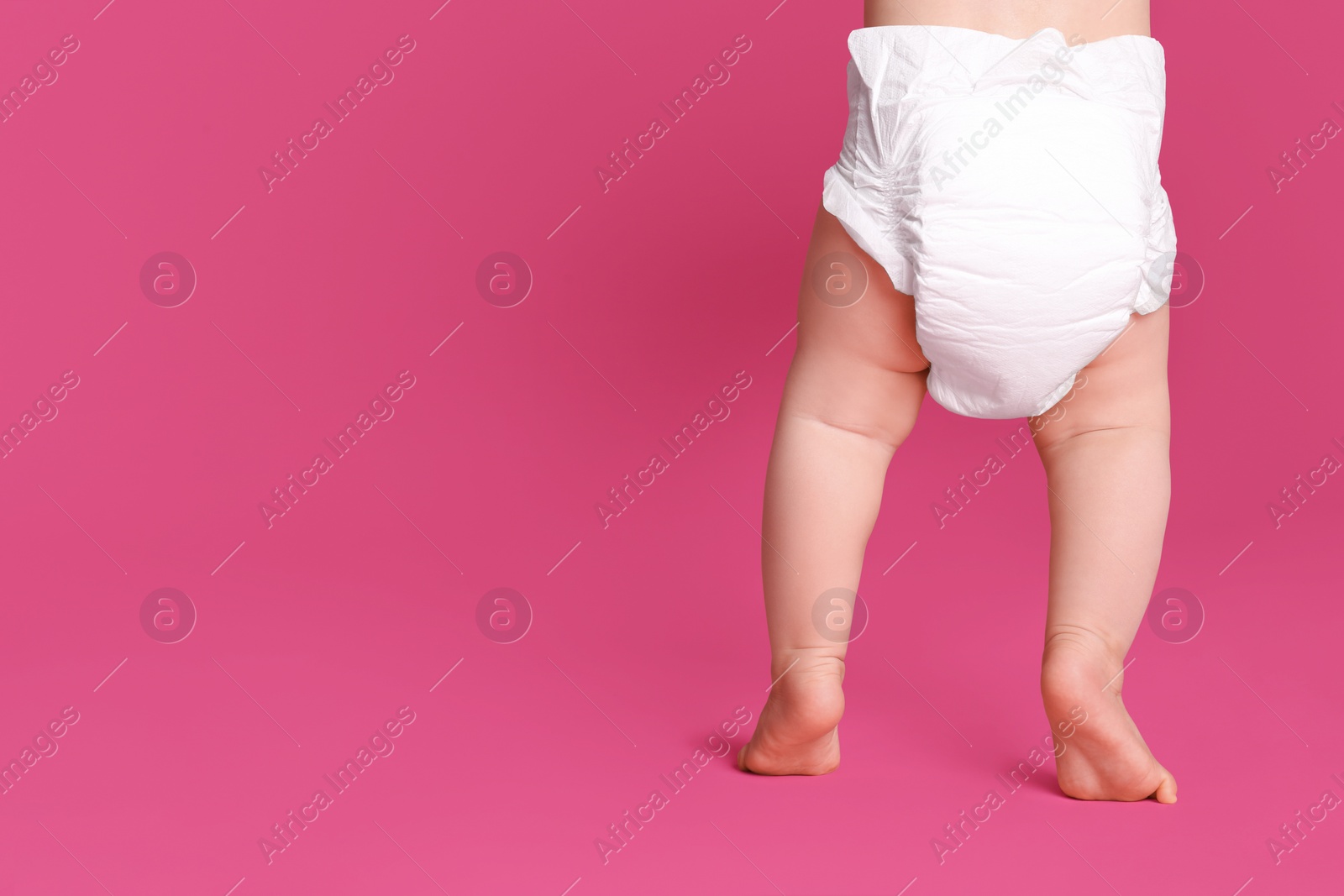 Photo of Back view of cute baby in dry soft diaper standing on pink background, closeup. Space for text