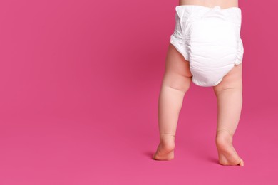 Back view of cute baby in dry soft diaper standing on pink background, closeup. Space for text