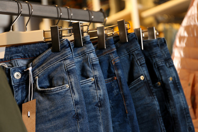 Modern jeans hanging on clothing rack in shop, closeup
