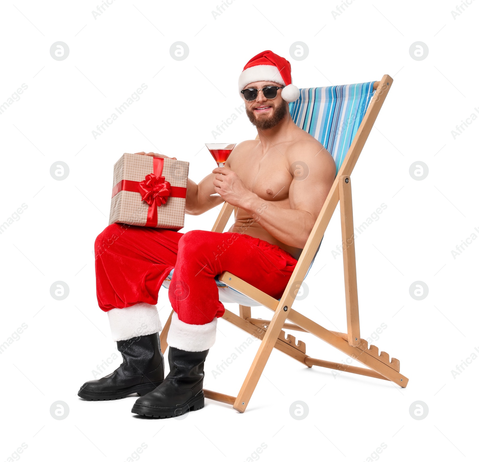 Photo of Muscular young man in Santa hat with deck chair, gift box, sunglasses and cocktail on white background