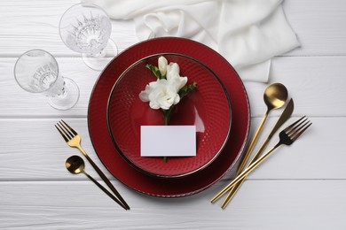 Stylish table setting. Dishes, cutlery, blank card and floral decor on white wooden background, flat lay