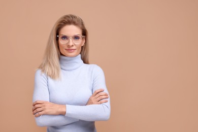 Photo of Portrait of beautiful middle aged woman in glasses with crossed arms on beige background. Space for text