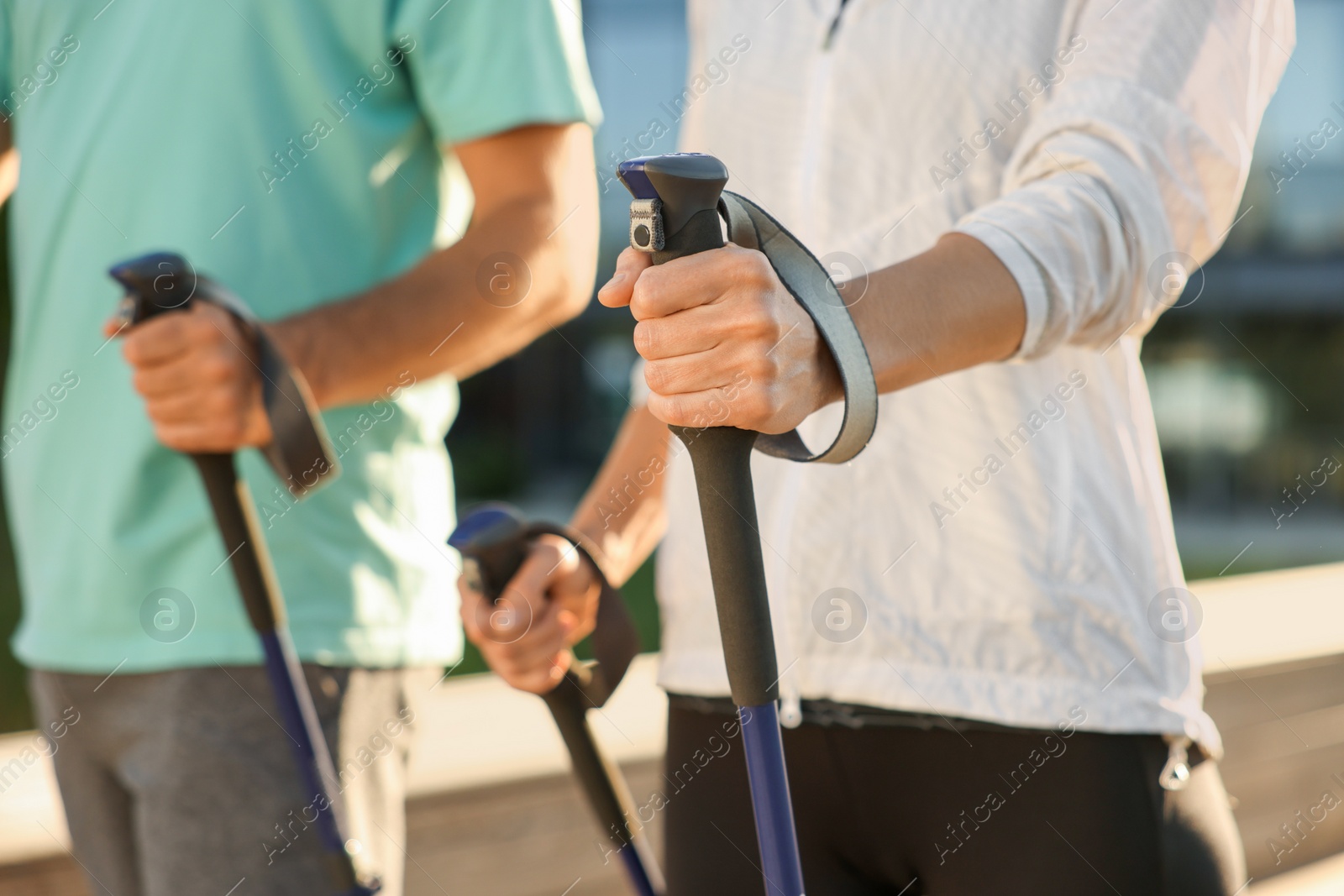 Photo of Couple practicing Nordic walking with poles outdoors, closeup