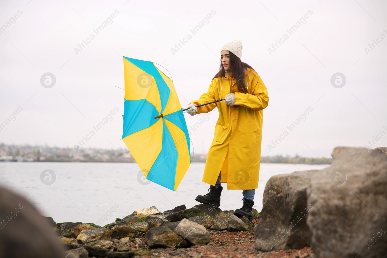 Photo of Woman in yellow raincoat with umbrella caught in gust of wind near river