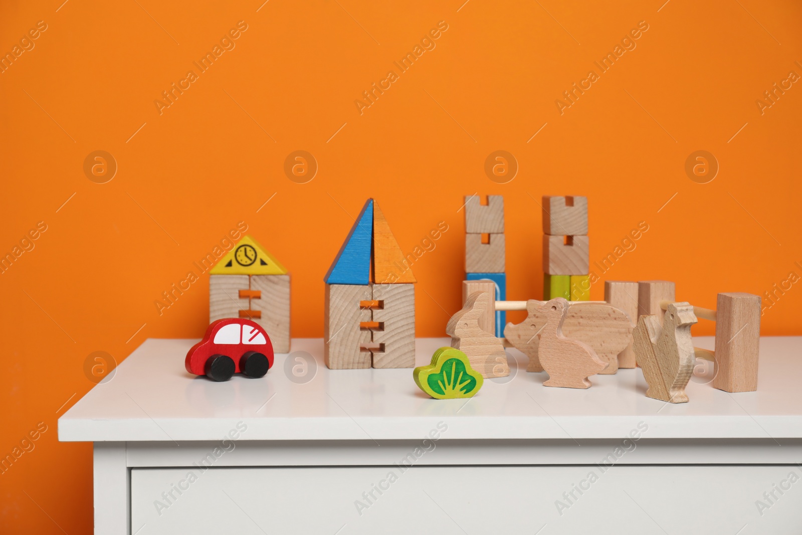 Photo of Set of wooden toys on white chest of drawers near orange wall, space for text. Children's development