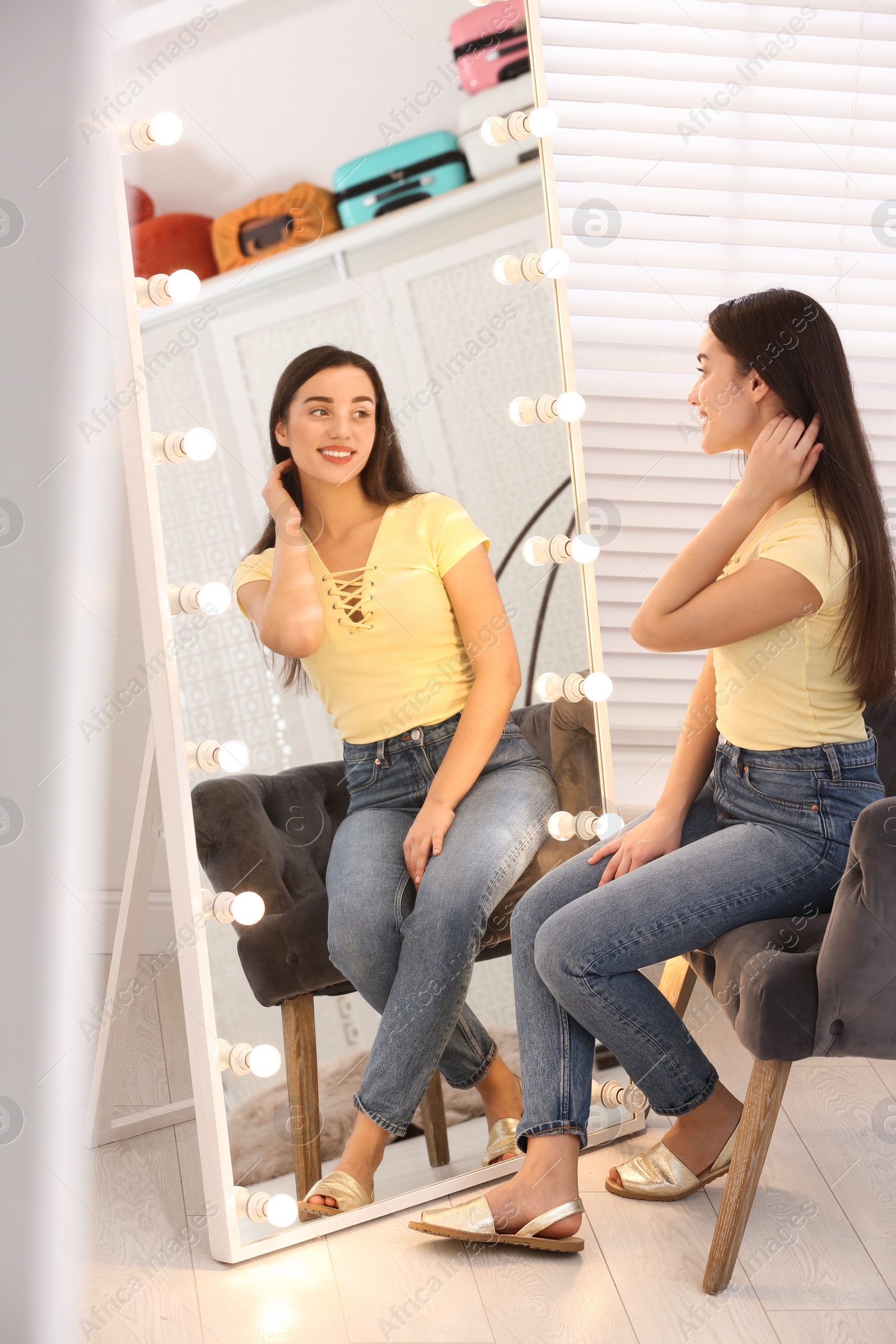 Photo of Beautiful young woman looking at herself in large mirror indoors