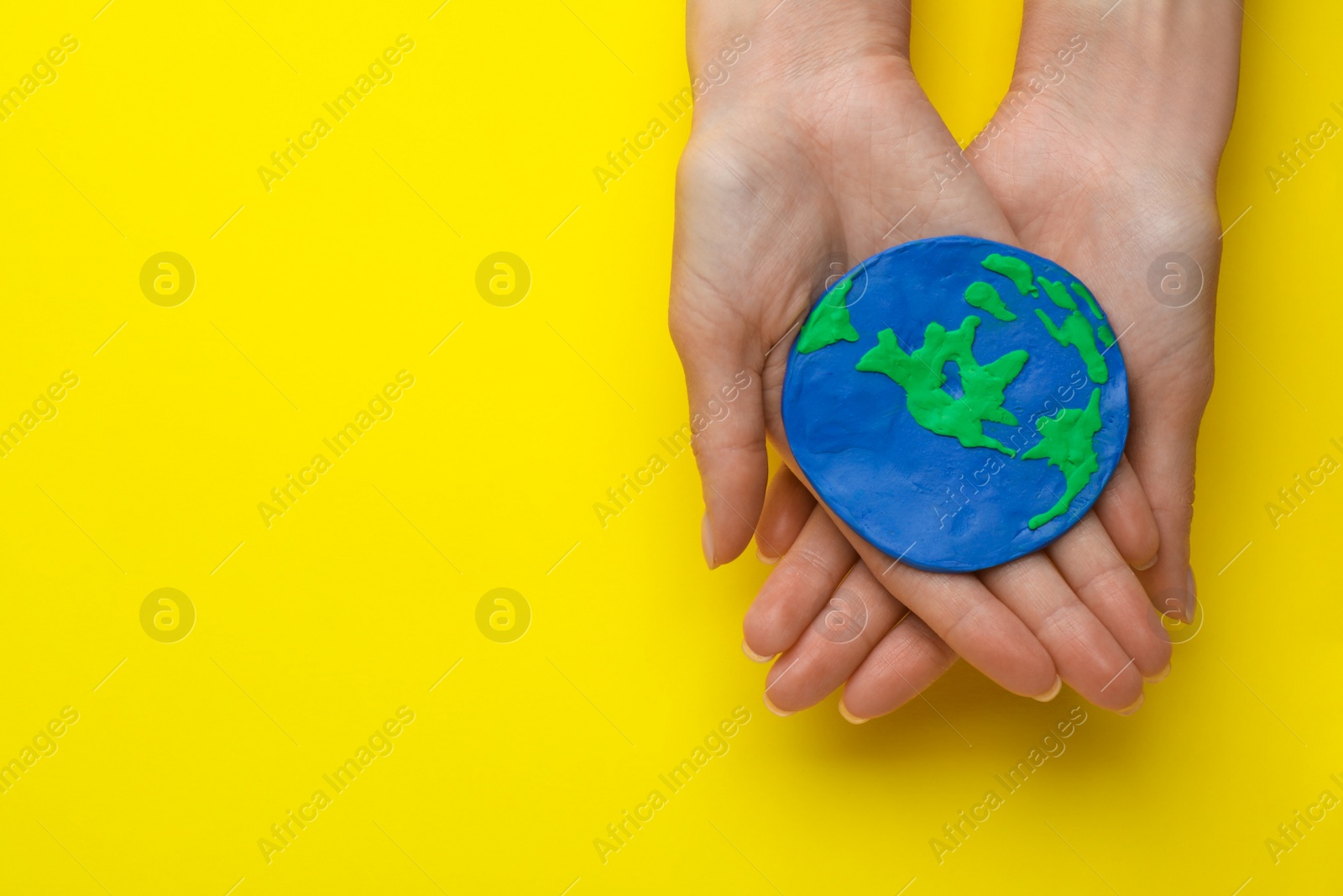 Photo of Woman holding plasticine model of planet on yellow background, top view with space for text. Earth Day