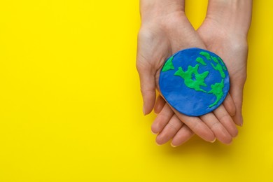 Photo of Woman holding plasticine model of planet on yellow background, top view with space for text. Earth Day