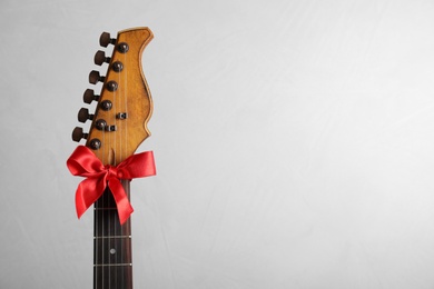Photo of Guitar with red bow on light background, space for text. Christmas music