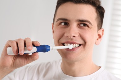 Photo of Man brushing his teeth with electric toothbrush indoors