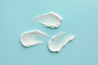 Photo of Samples of face cream on light blue background, top view