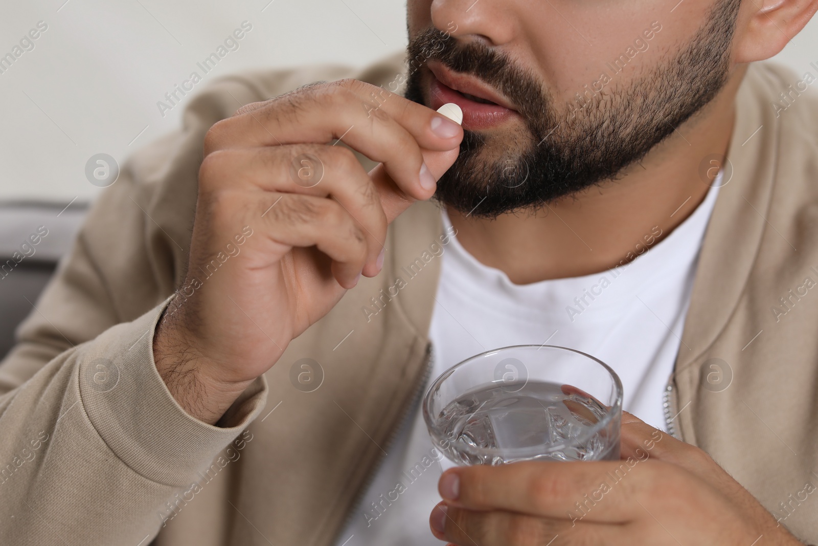 Photo of Man with glass of water taking antidepressant pill on blurred background, closeup