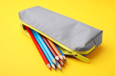 Many colorful pencils in pencil case on yellow background, closeup