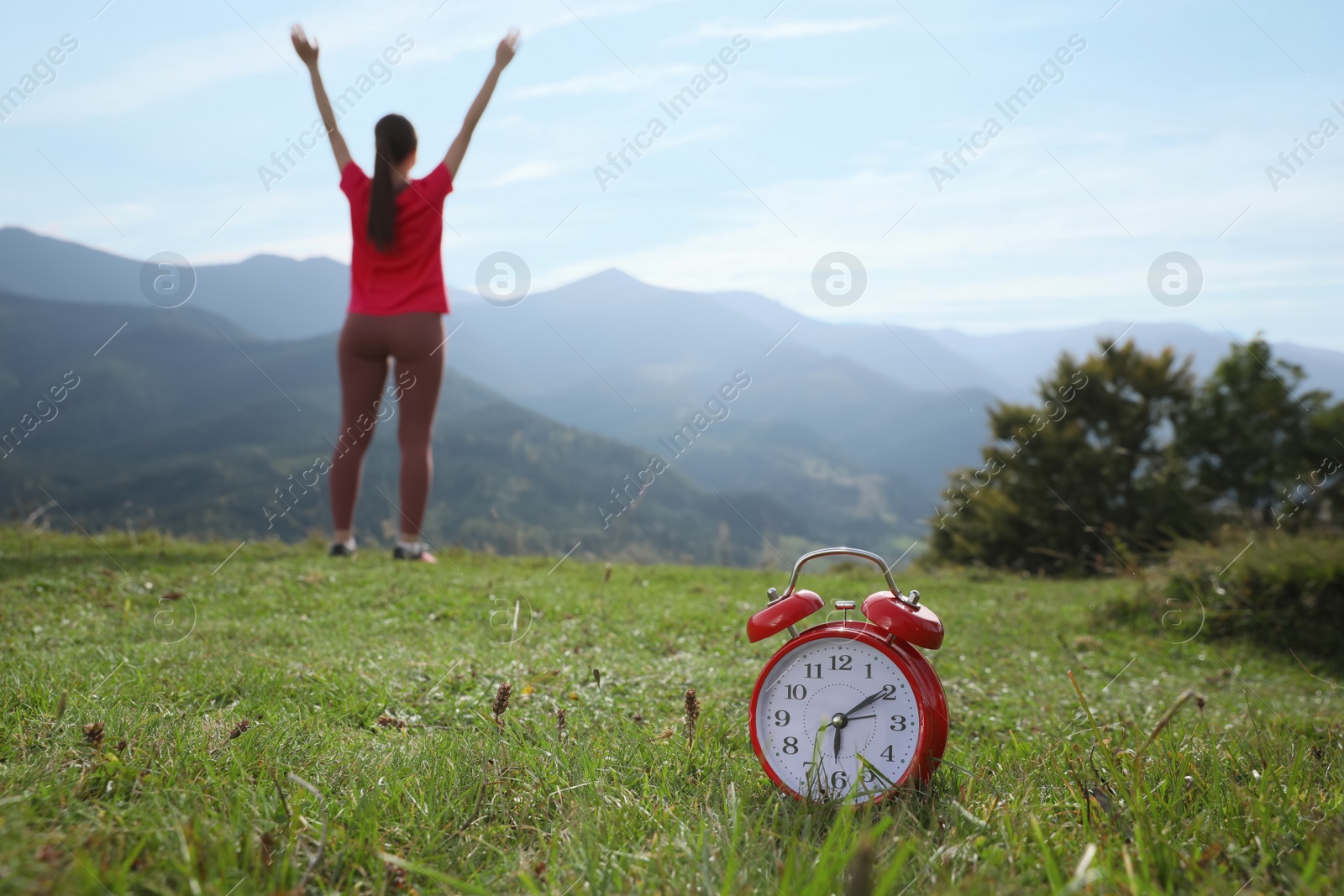 Photo of Woman doing morning exercise in mountains, focus on alarm clock