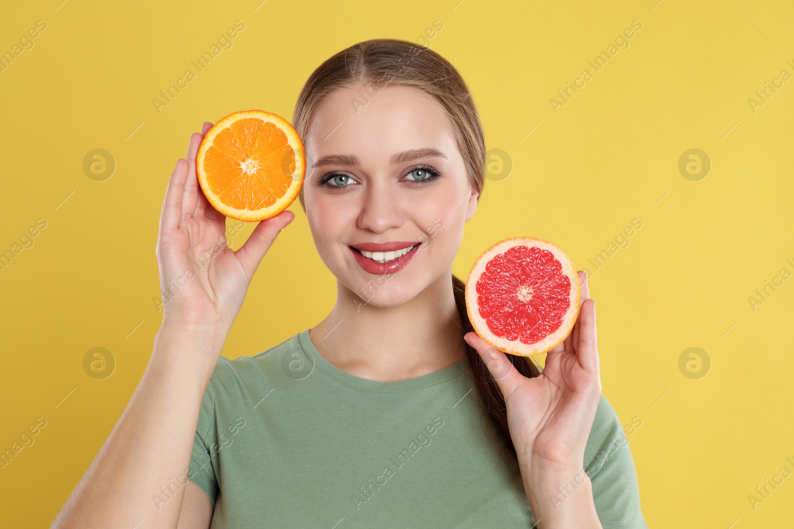 Photo of Young woman with cut orange and grapefruit on yellow background. Vitamin rich food