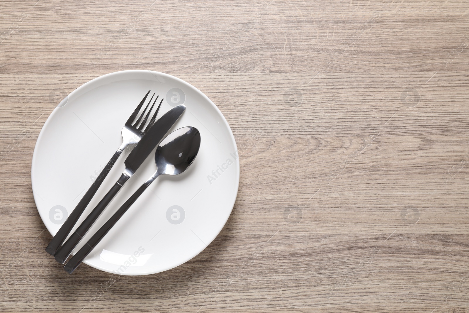 Photo of Plate with shiny silver cutlery on wooden table, top view. Space for text