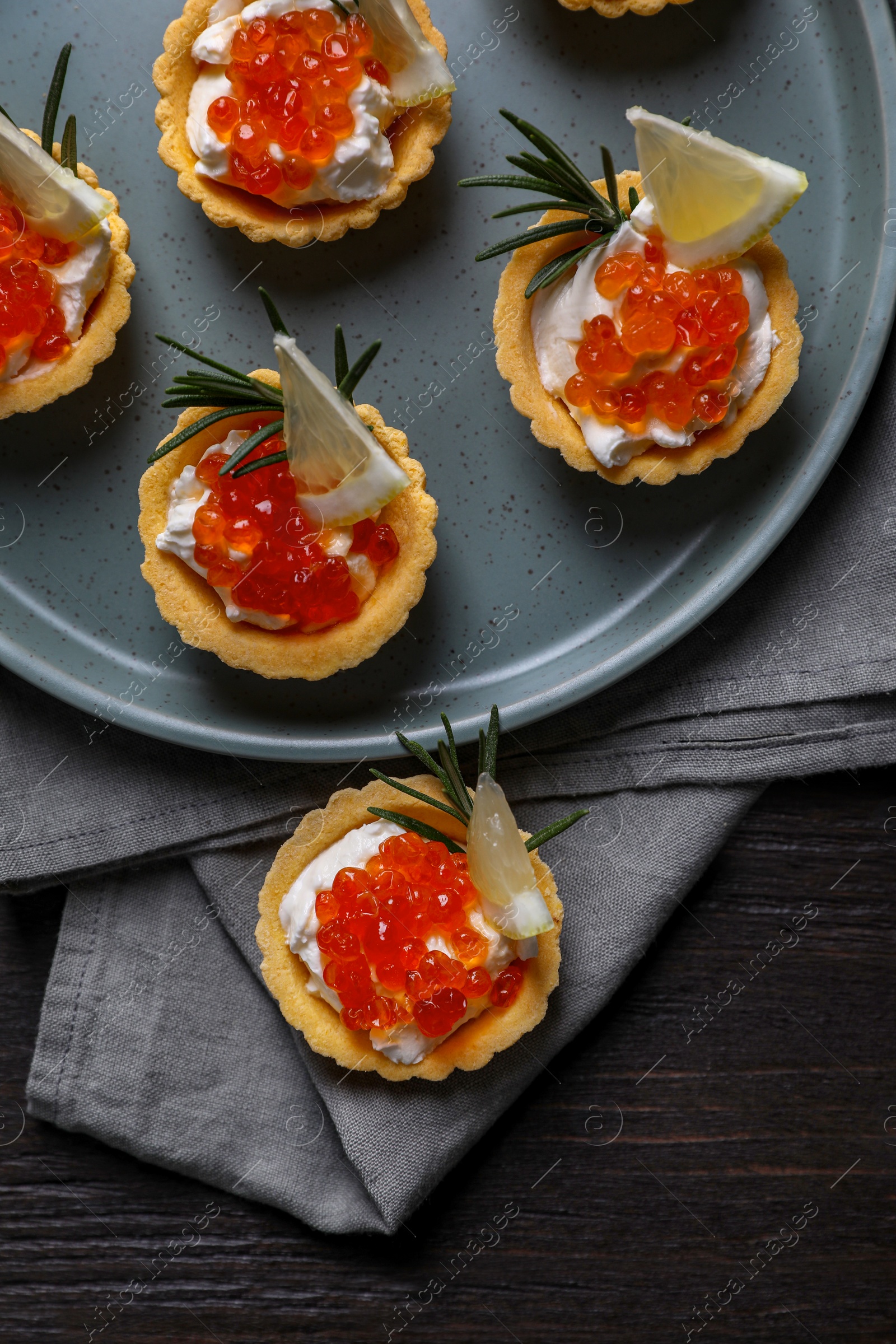 Photo of Delicious tartlets with red caviar and cream cheese served on wooden table, top view