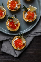 Delicious tartlets with red caviar and cream cheese served on wooden table, top view