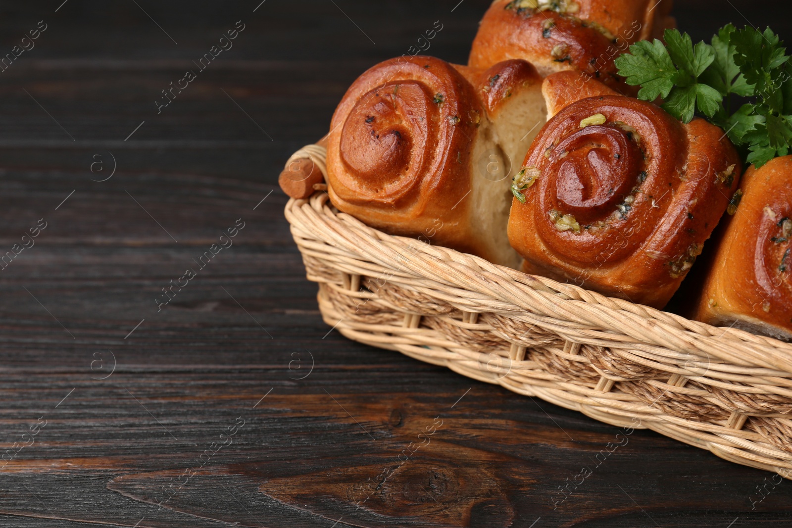 Photo of Delicious pampushky (buns with garlic) in wicker basket on wooden table, space for text