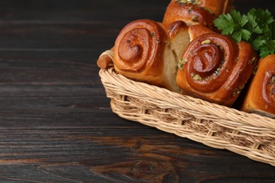 Photo of Delicious pampushky (buns with garlic) in wicker basket on wooden table, space for text