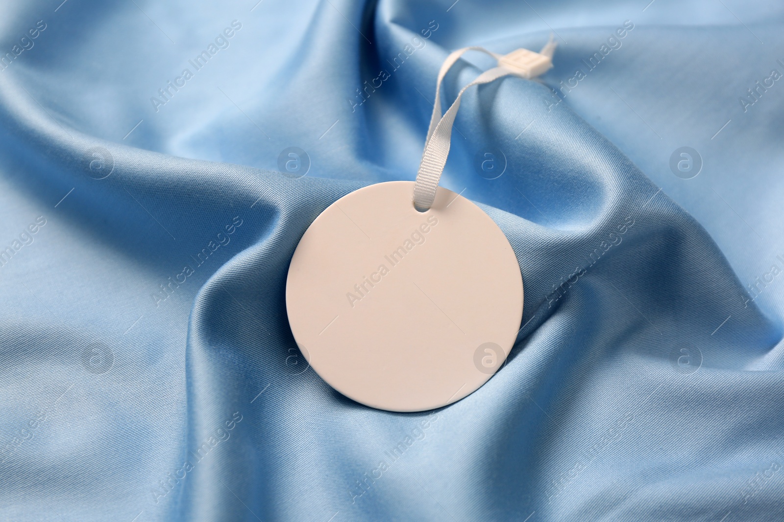 Photo of Blank white tag on light blue silky fabric, closeup. Space for text