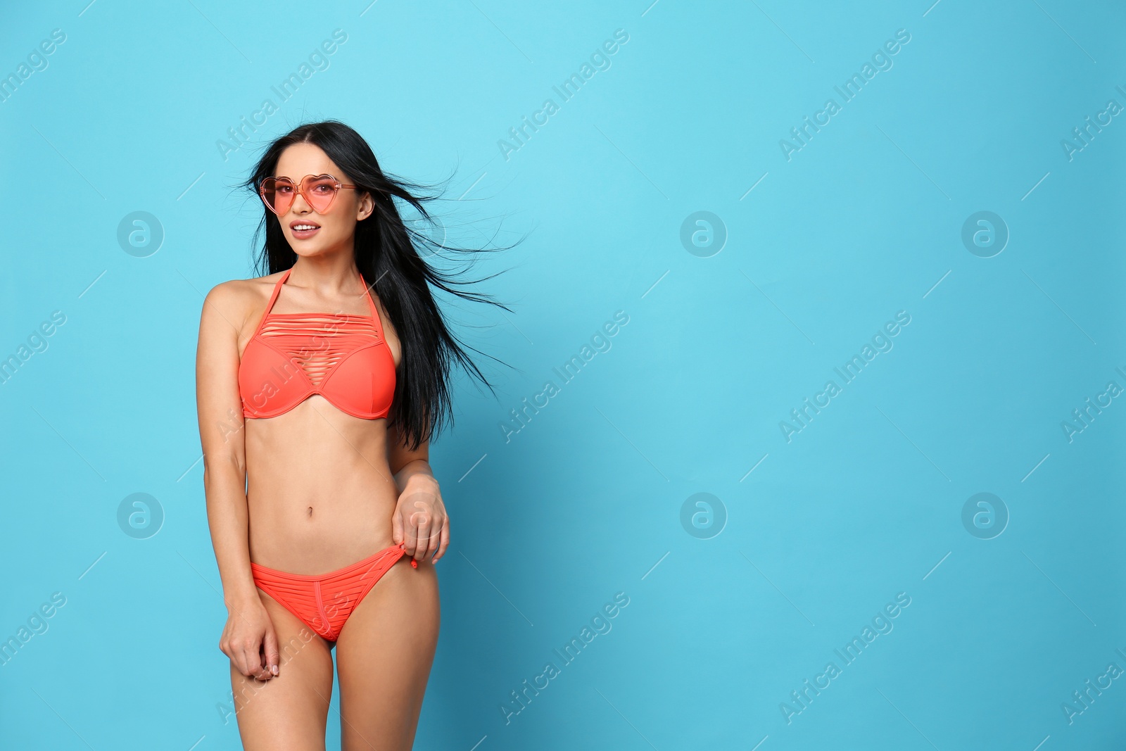 Photo of Beautiful young woman in stylish bikini with sunglasses on light blue background. Space for text