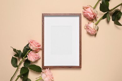 Empty photo frame and beautiful flowers on beige background, flat lay. Space for design