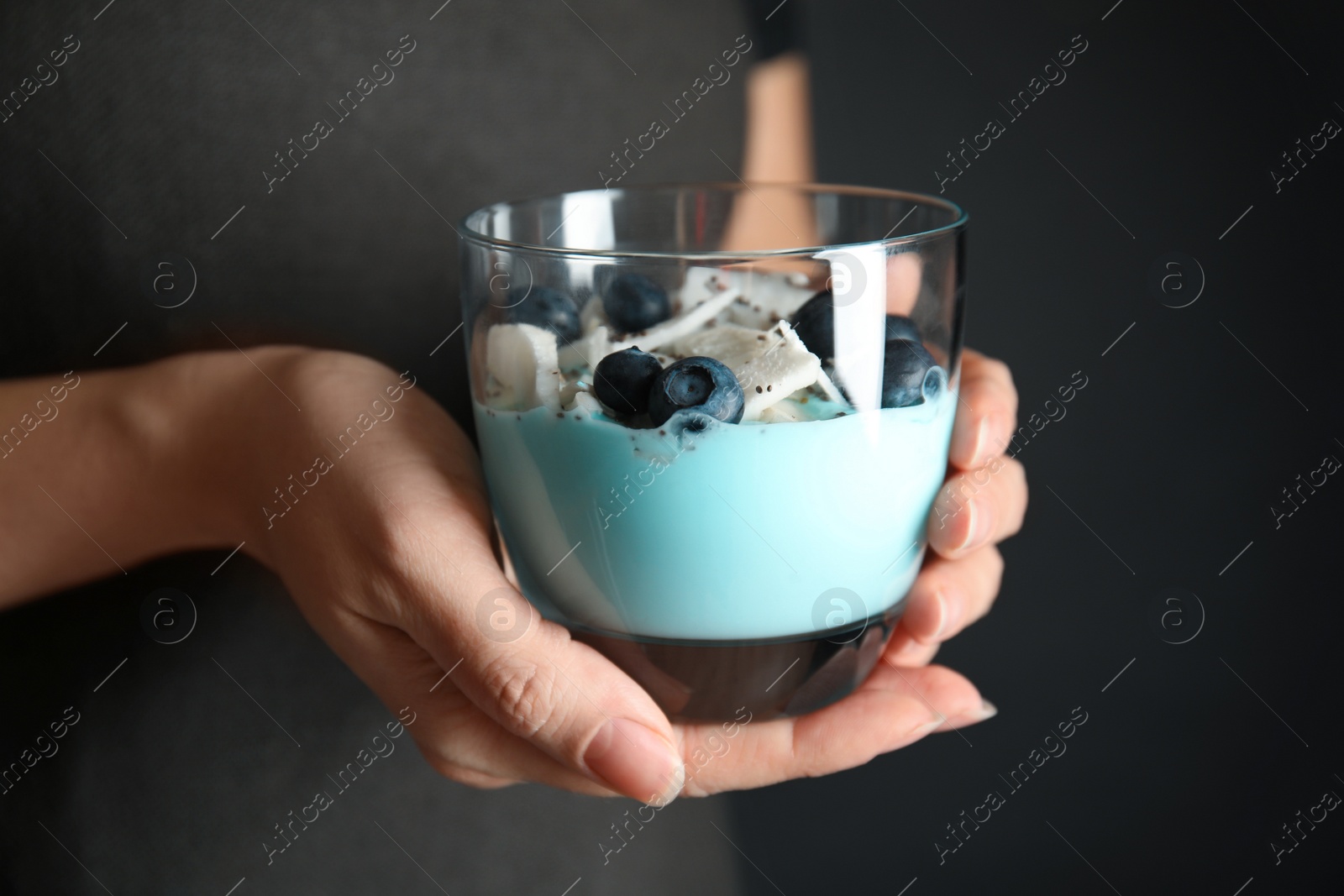 Photo of Woman holding glass cup of spirulina smoothie on dark background, closeup