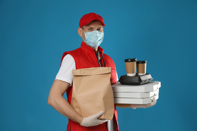 Photo of Courier in protective mask and gloves holding order on blue background. Food delivery service during coronavirus quarantine