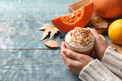 Woman holding glass cup of tasty pumpkin spice latte on wooden table, closeup with space for text