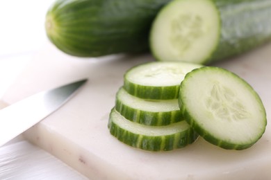 Photo of Cucumbers, knife and marble cutting board on white table, closeup