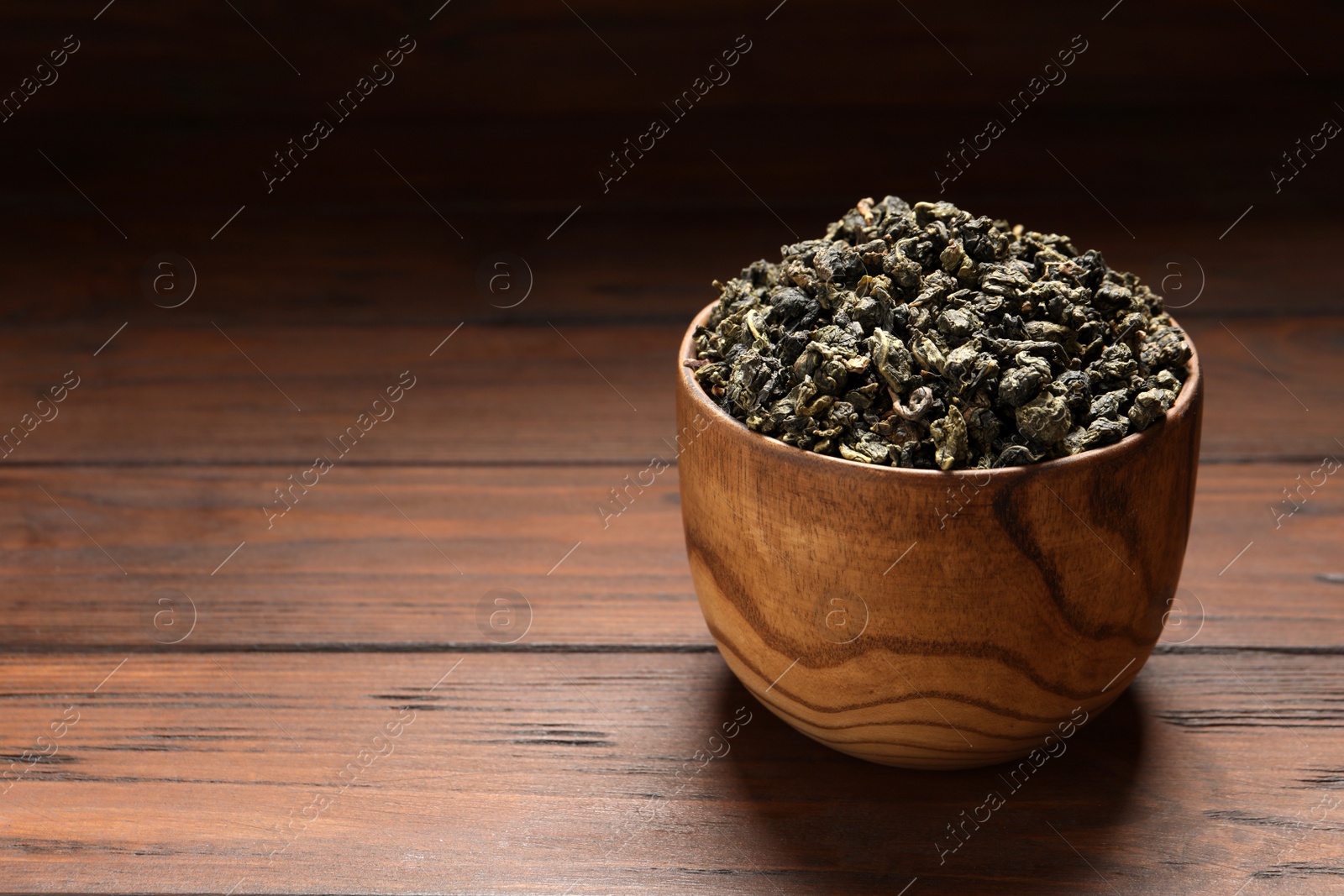 Photo of Bowl of Tie Guan Yin oolong tea leaves on wooden table. Space for text