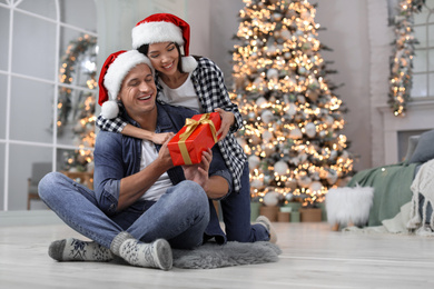 Happy young couple in Santa hats with Christmas gift at home