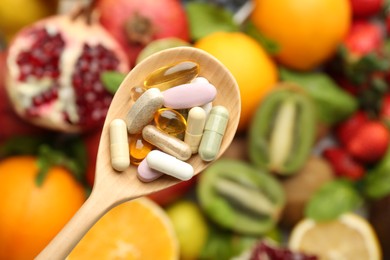 Photo of Different vitamin pills in spoon over fresh fruits, top view. Space for text