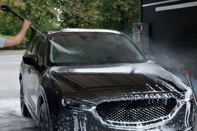 Photo of Man washing auto with high pressure water jet at car wash, closeup