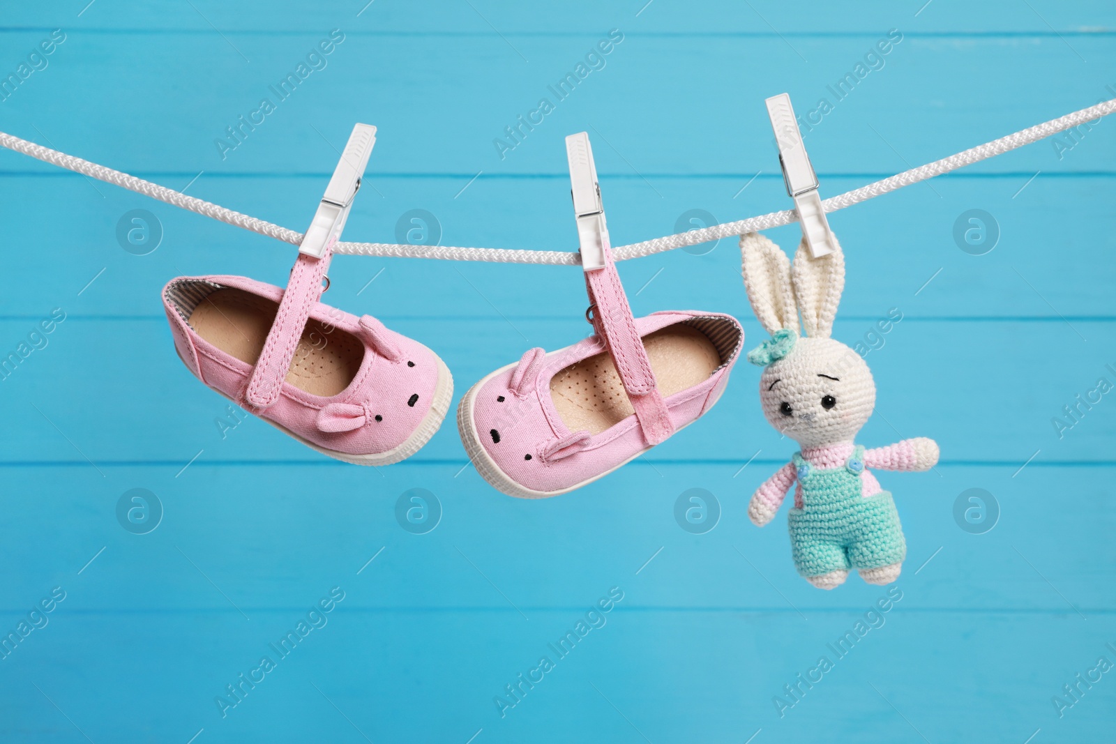 Photo of Cute baby shoes and crochet toy drying on washing line against light blue wooden wall