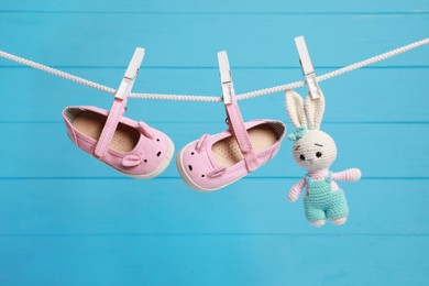 Photo of Cute baby shoes and crochet toy drying on washing line against light blue wooden wall