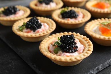 Photo of Delicious canapes with salmon and caviar on black table, closeup