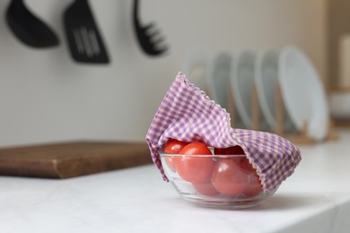 Photo of Tomatoes in bowl covered with beeswax food wrap on white table indoors, space for text