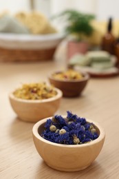 Photo of Bowls of dry flowers on light wooden table. Spa therapy