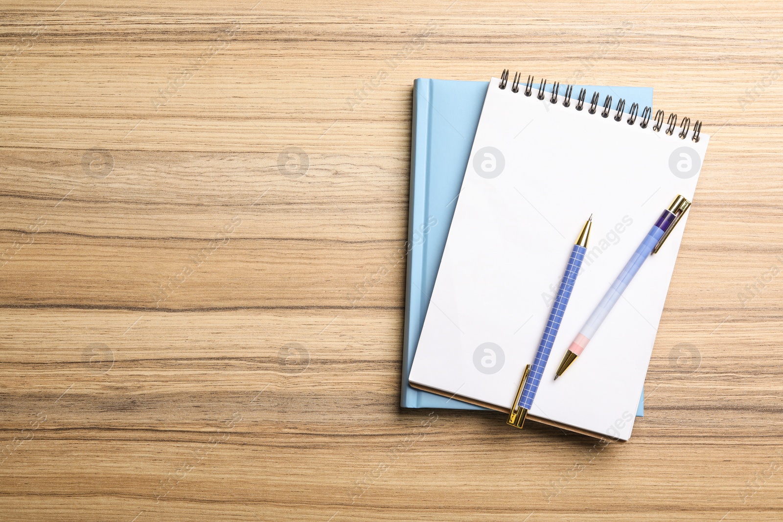 Photo of Stylish notebooks and pens on wooden table, top view. Space for text