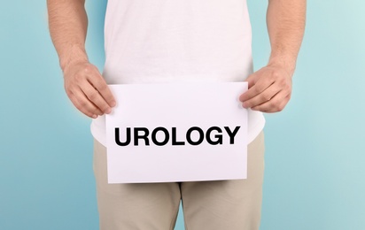 Young man holding paper with word UROLOGY on color background