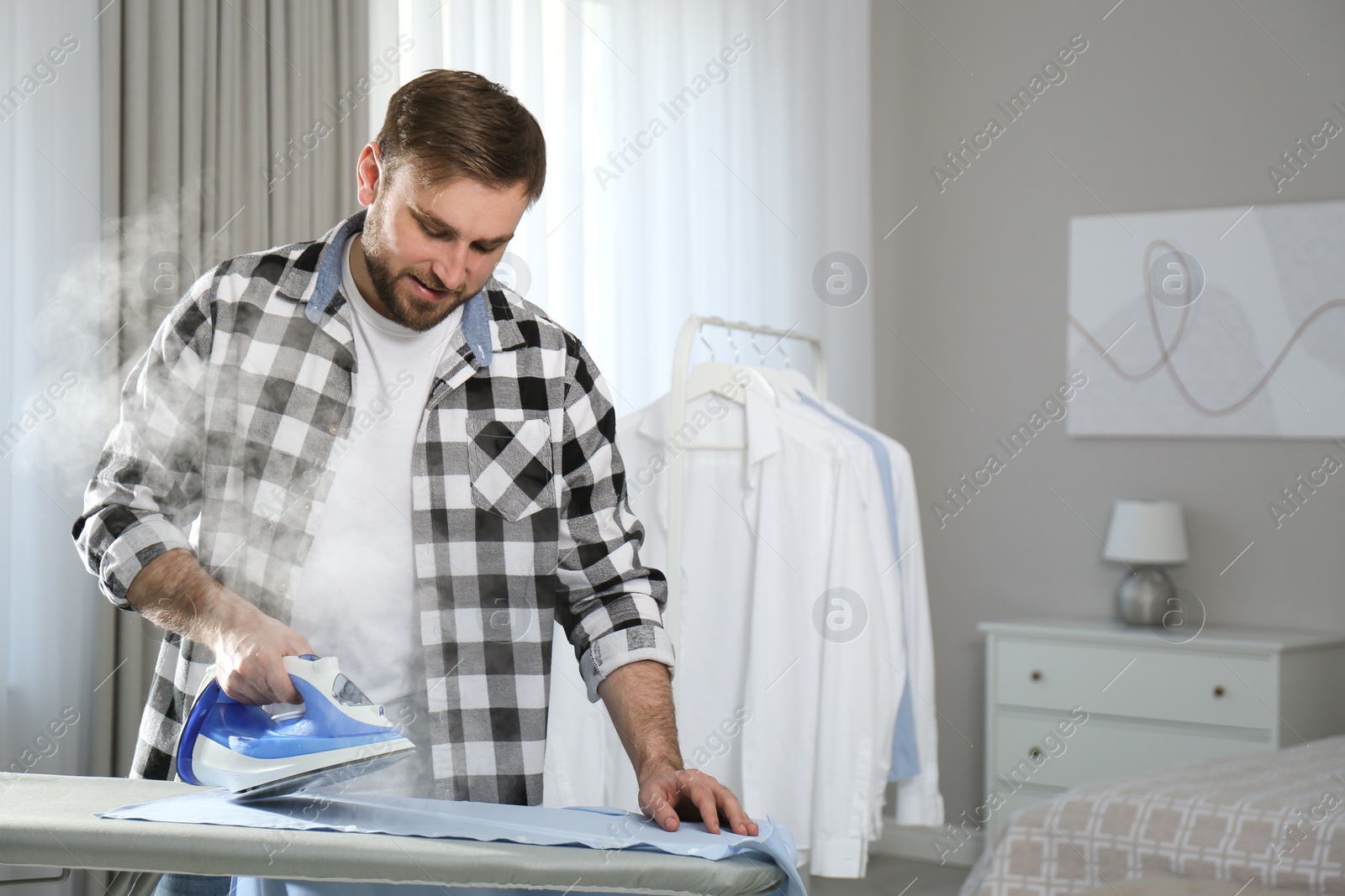 Photo of Young man ironing clean shirt at home