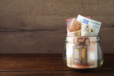 Image of Glass jar full of money on wooden table. Space for text 