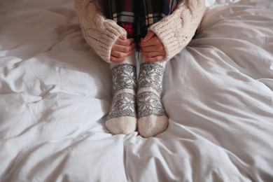 Photo of Woman wearing knitted socks on bed with soft blanket, closeup