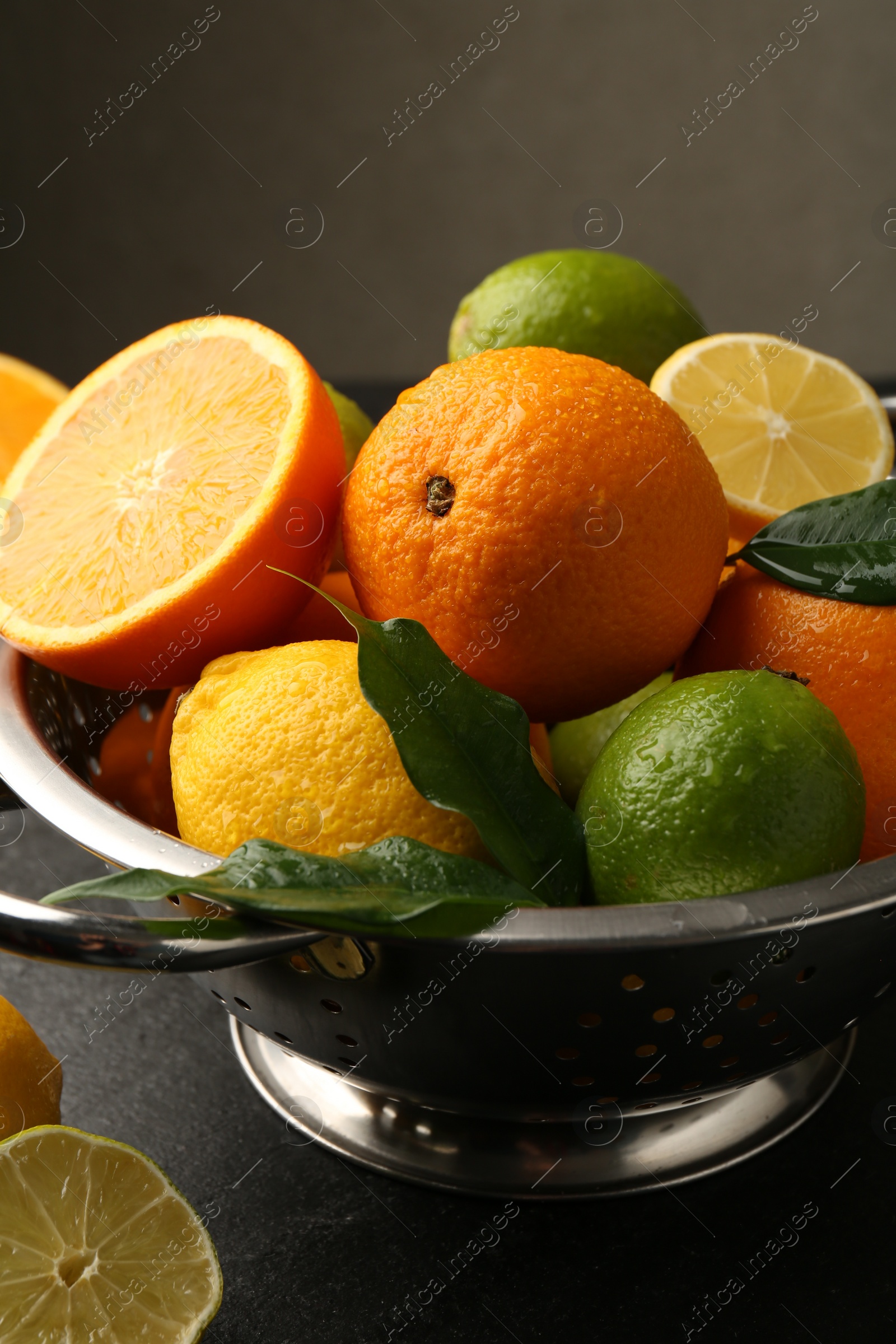 Photo of Fresh citrus fruits in colander on dark table, closeup