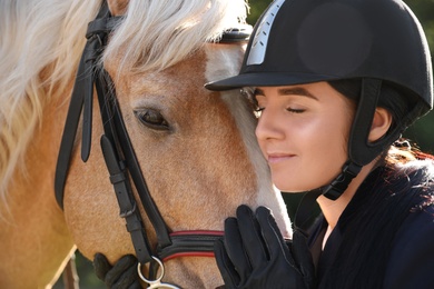 Photo of Young woman in horse riding suit and her beautiful pet outdoors on sunny day, closeup